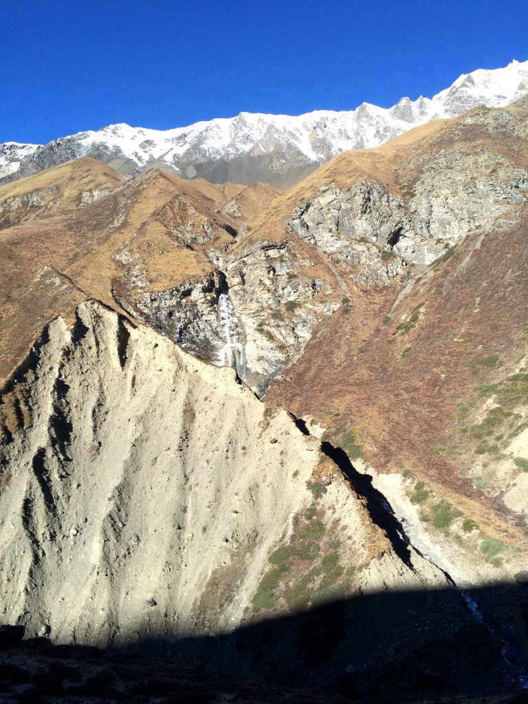 The dry high-altitude terrain of the Manang side of the Annapurna Circuit with distant snow-capped peaks.