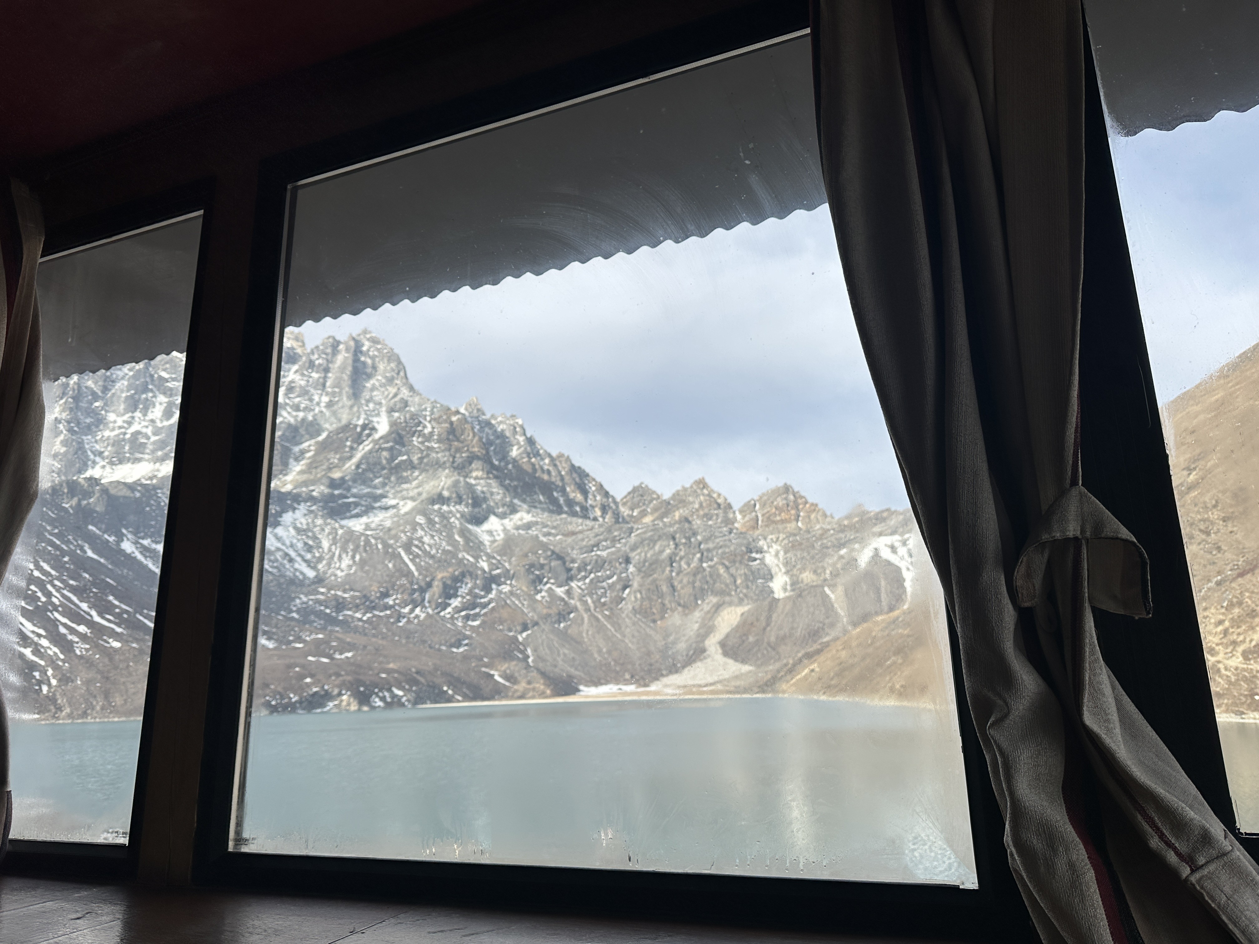 View of Gokyo Lake and the surrounding peaks through a teahouse window.