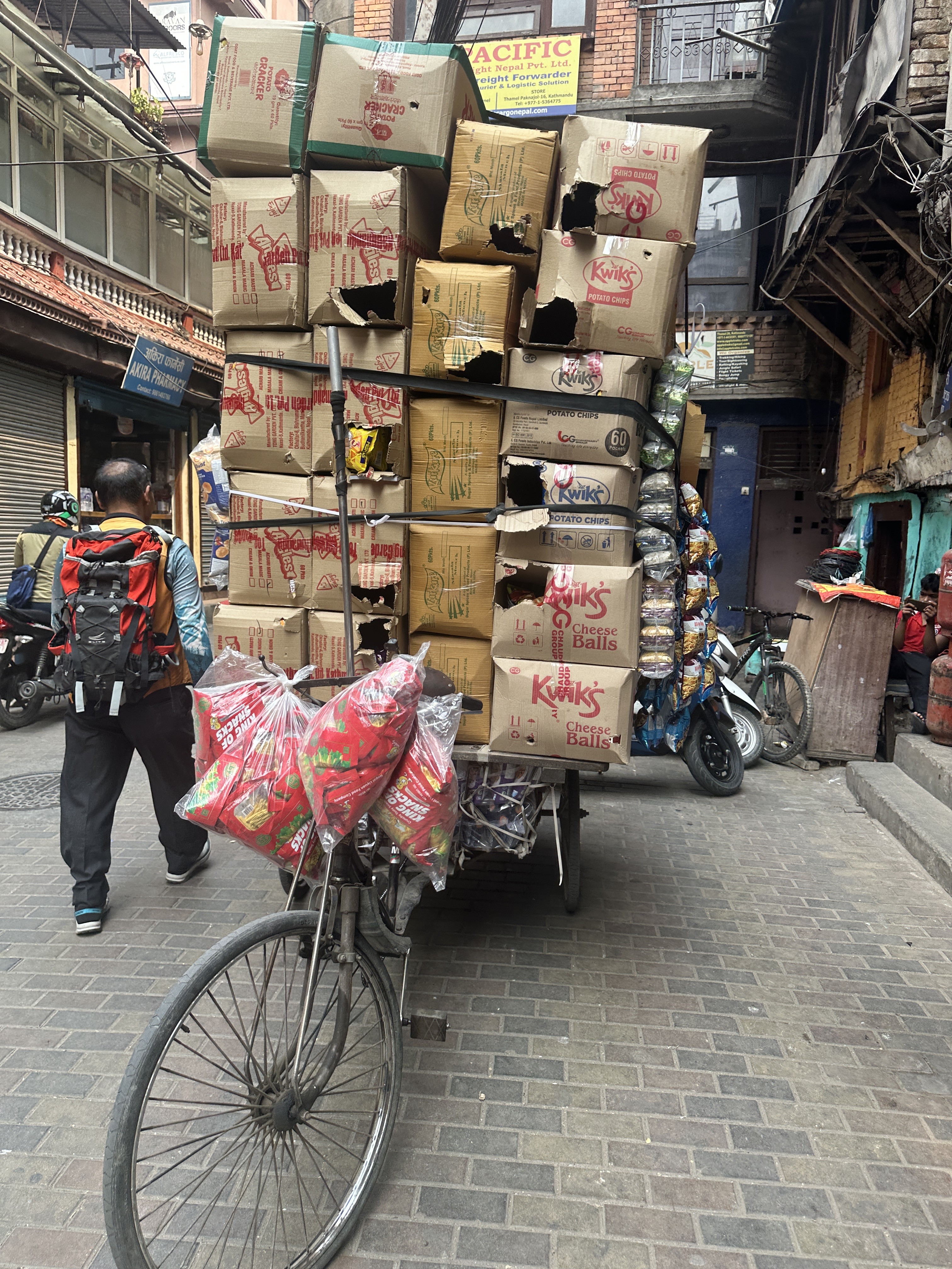 A delivery porter with stacked noodle boxes in a narrow Kathmandu street.